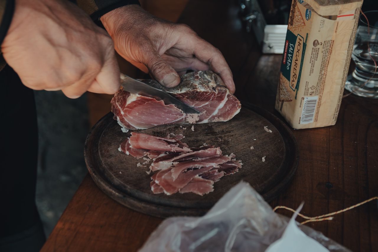 A hand expertly slices cured ham on a wooden board, capturing the essence of rustic food preparation.