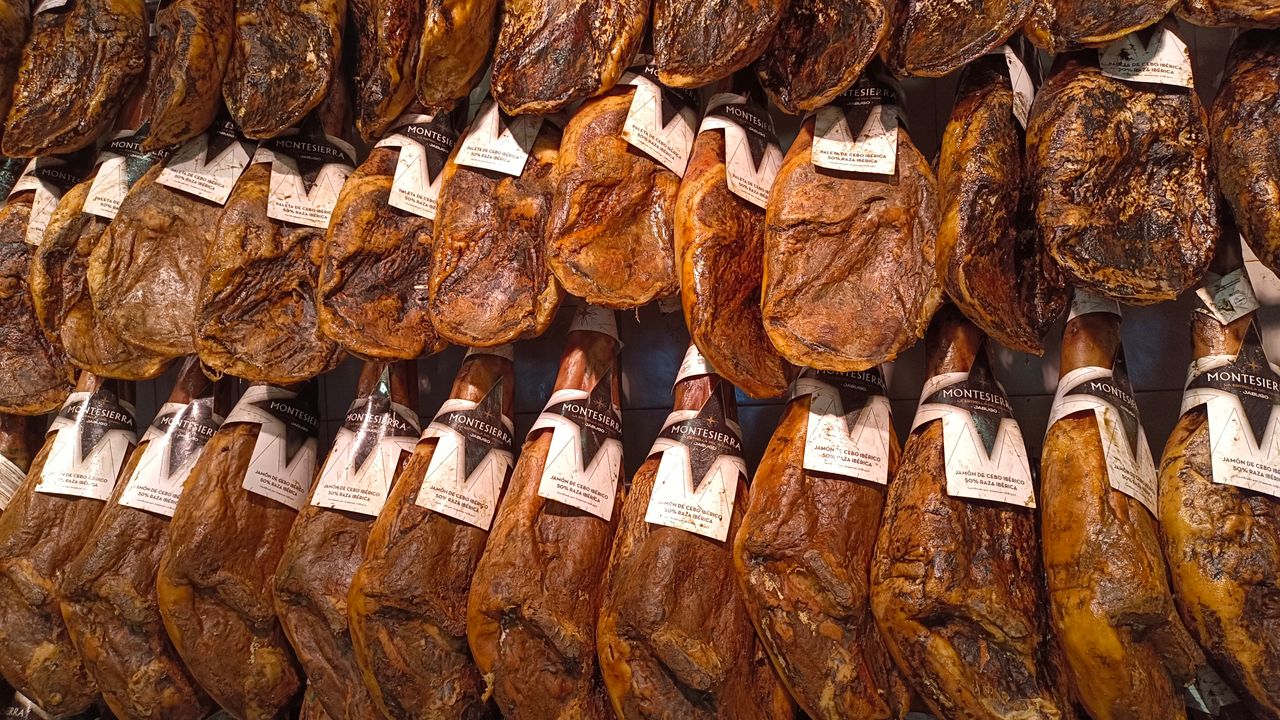 Close-up of numerous cured ham legs with labels hanging in a traditional market.